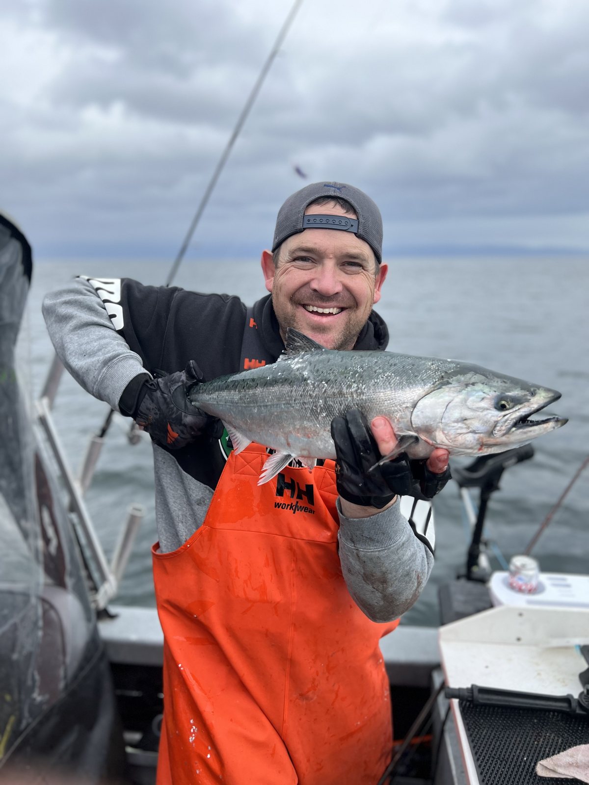 Jeremy Russell holding a bright chrome salmon in the boat, open water behind him.